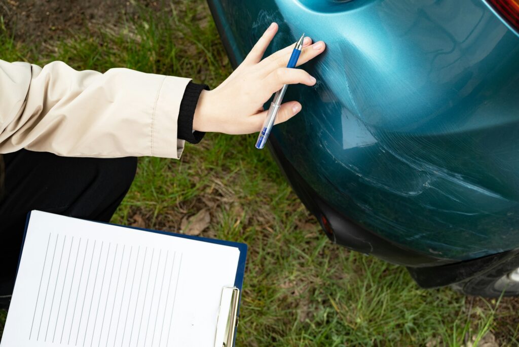 A close-up of a damaged car bumper with a person filling out a form on a tablet, getting insurance.